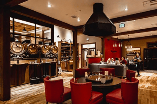 Cozy restaurant with red chairs, round tables, and patrons dining, wooden floors and brewery tanks in background.