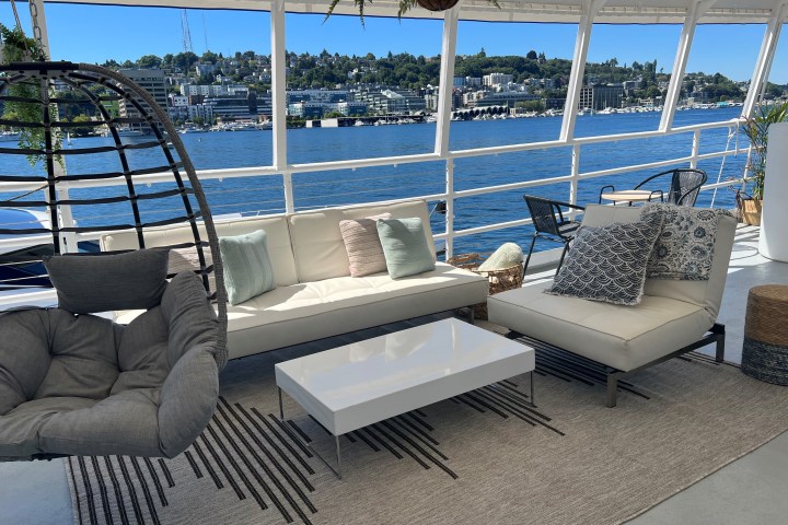 Modern boat deck with cushioned seating, hanging chair, and lake view under a clear blue sky.
