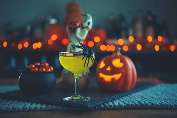 Halloween cocktail with spider, pumpkin, and candies on table.