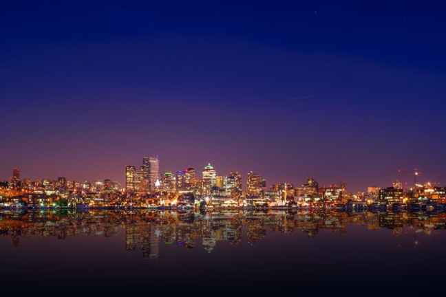 Seattle skyline at night with city lights and Space Needle reflection on water.