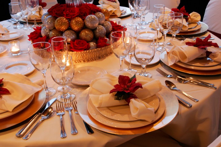 Elegant table setup with red roses, glittery ornaments, gold plates, and glassware for a formal dinner.