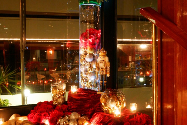 Festive decorations with roses, candles, gold ornaments, and a nutcracker on a red cloth.