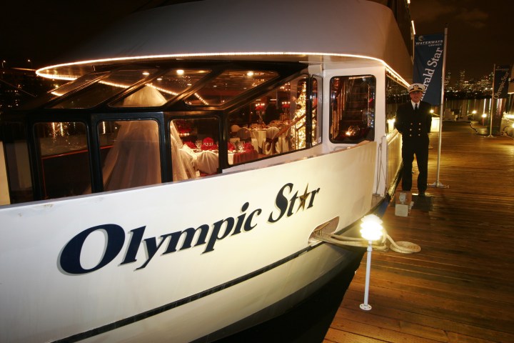 Docked yacht 'Olympic Star' at night with lights, a crew member, and an elegant interior visible.