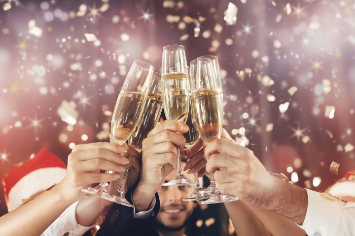 Hands toasting with champagne glasses, confetti falling in festive atmosphere.