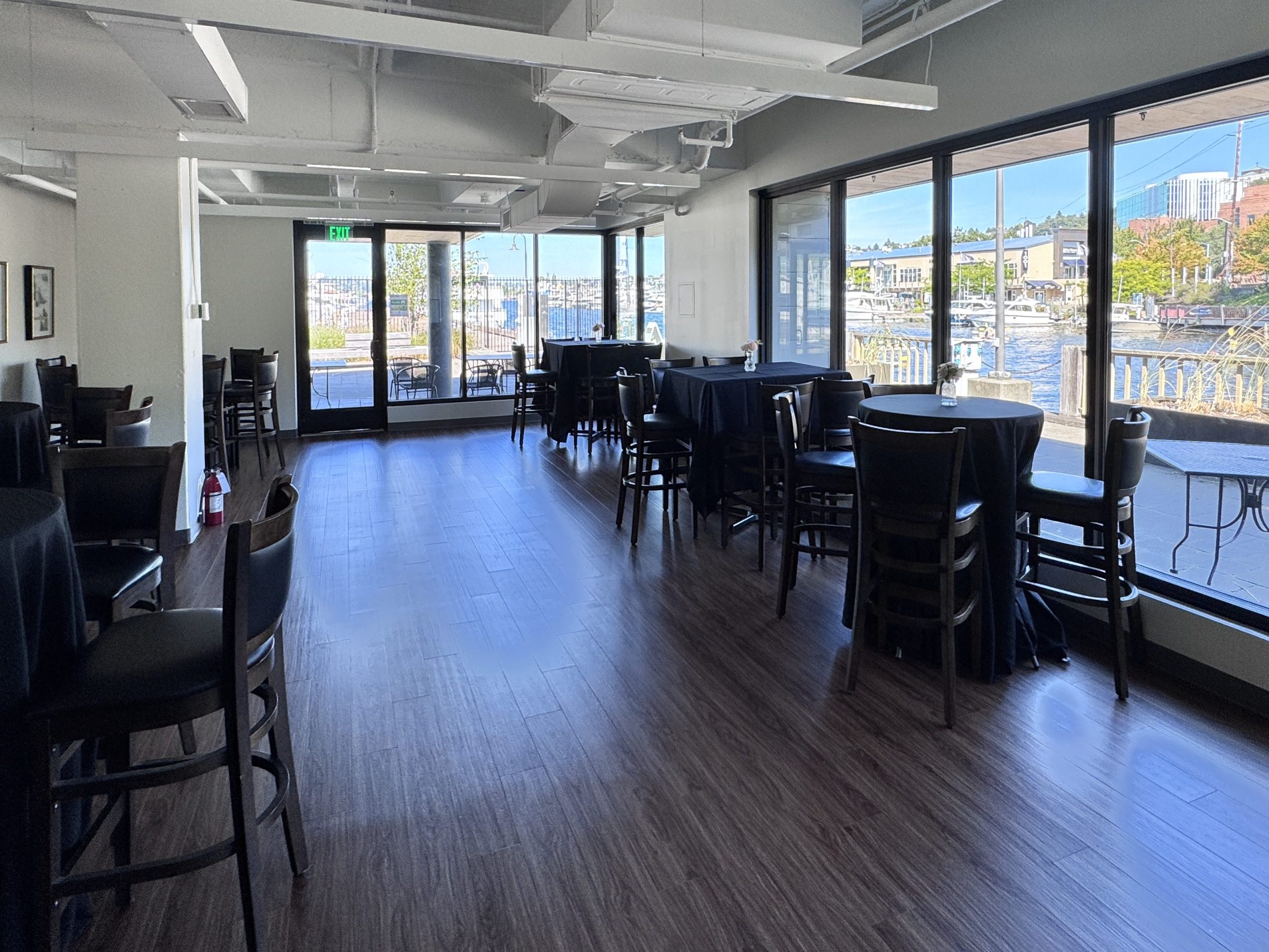 Empty event space with tables, chairs, and large windows overlooking a marina.